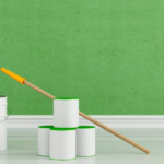 painting banner | Top Rated Painters Oxford | Art Evans & Sons Several white paint cans, a paint roller with a yellow handle, paint trays, and bottles of colored paint are arranged on a shiny floor in front of a freshly painted green wall.