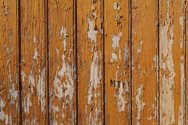 Close-up of weathered wood fence showing peeling stain and moisture damage from freeze-thaw cycles